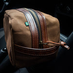 Necessaire Lona Encerada e Couro Marrom, still sobre superfície neutra – DANTE Capelli